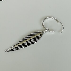 Puede incluir: Pendiente de aro de plata con un dije de pluma. La pluma est&aacute; detallada con l&iacute;neas y tiene un acabado plateado.