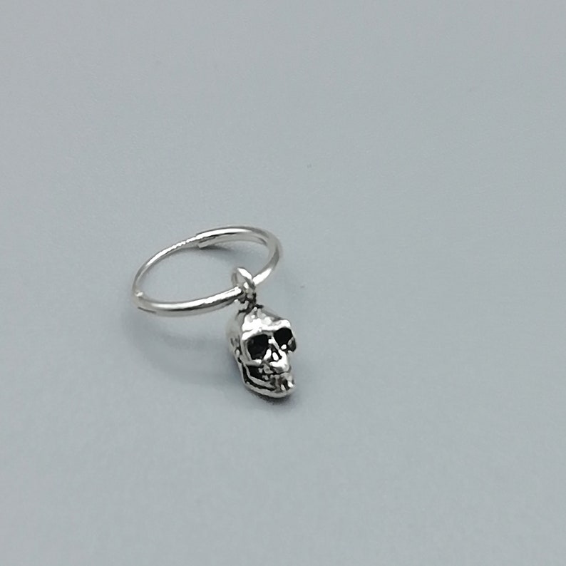Pu&ograve; includere: Orecchini a cerchio d'argento con un piccolo ciondolo a forma di teschio appeso all'anello.