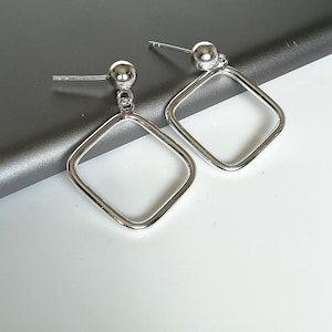 May include: A pair of silver earrings with square hoops and small round balls at the top.