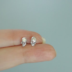 May include: A pair of silver skull stud earrings. The earrings are small and delicate, and they are perfect for adding a touch of edgy style to any outfit.