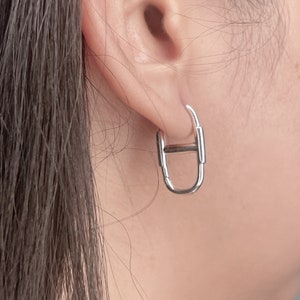May include: Silver hoop earrings with a unique, geometric design. The earrings are made of a smooth, polished metal and have a simple, modern look.