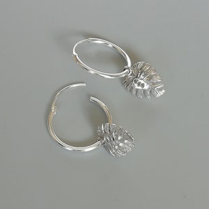 May include: A pair of silver hoop earrings with a leaf-shaped charm hanging from each hoop.