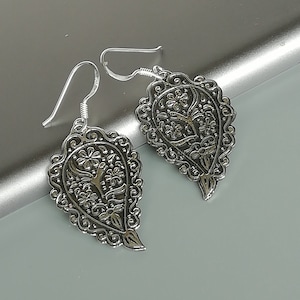 Op de afbeelding: Een paar zilveren oorhangers met een paisley-ontwerp. De oorbellen zijn ingewikkeld en gedetailleerd, met een bloemenpatroon.