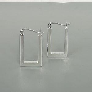 Könnte beinhalten: Ein Paar silberne quadratische Creolen. Die Ohrringe sind schlicht und elegant.