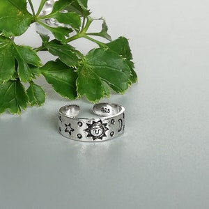 May include: Silver adjustable toe ring with a sun, moon, and stars design. The ring is marked with the number "925" on the inside.