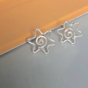 Può includere: Un paio di orecchini a forma di stella in argento con un design a spirale al centro.