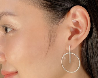 May include: Silver hoop earrings with a vertical bar hanging from the hoop.