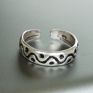 May include: Silver toe ring with a wavy black and white design.