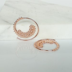May include: A pair of rose gold spiral hoop earrings with a delicate, intricate design.