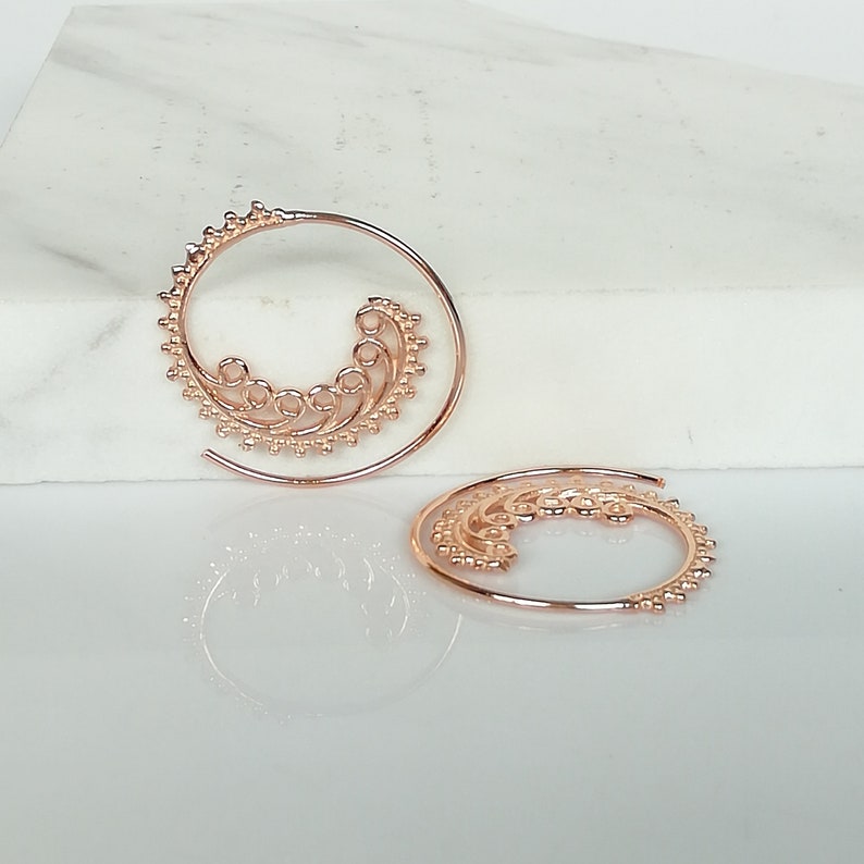 May include: A pair of rose gold spiral hoop earrings with a delicate, intricate design.