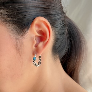 Puede incluir: Pendientes de aro de plata con un acento de piedra turquesa. Los pendientes están detallados con un diseño floral.