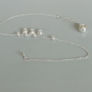 Puede incluir: Tobillera de cadena plateada con un pequeño dije de campana y tres dijes de concha.