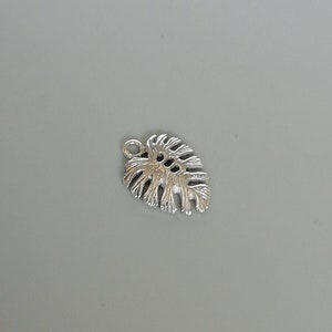 May include: Silver charm in the shape of a monstera leaf. The leaf has a detailed design with cutouts.