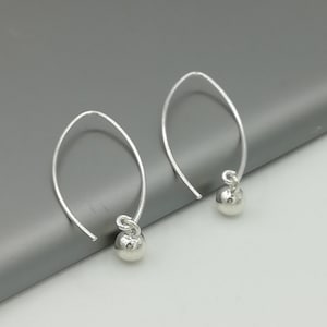 May include: A pair of silver hoop earrings with a small ball charm hanging from each hoop.