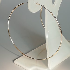 May include: A pair of gold hoop earrings on a white display stand. The earrings are large and circular.