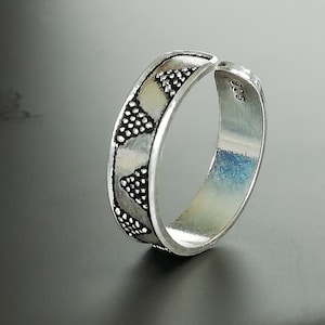 May include: Silver toe ring with a geometric pattern. The ring is open and adjustable.