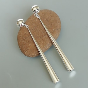 Puede incluir: Un par de pendientes de plata con una bola redonda en la parte superior y un diseño largo, puntiagudo y cónico.