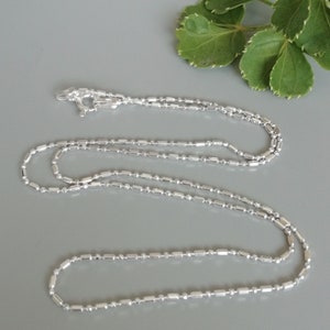 Può includere: Una collana a catena d'argento con un design a catena a scatola. La catena è composta da piccoli anelli rettangolari.