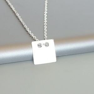 May include: A silver chain necklace with a square pendant. The pendant has two small holes in it.