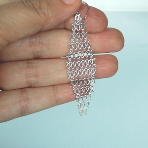 Könnte beinhalten: Silberne Kettenohrringe mit geometrischem Design. Die Ohrringe sind lang und hängen vom Ohrläppchen.