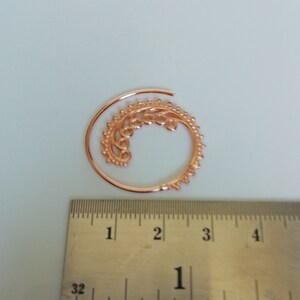 May include: A rose gold spiral ear cuff with a delicate floral design. The cuff is approximately 1 inch in diameter.