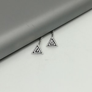 May include: A pair of silver triangle stud earrings with a black geometric design.