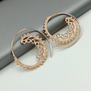 May include: A pair of gold-toned hoop earrings with a delicate, swirling design. The earrings are made of metal and have a textured finish.