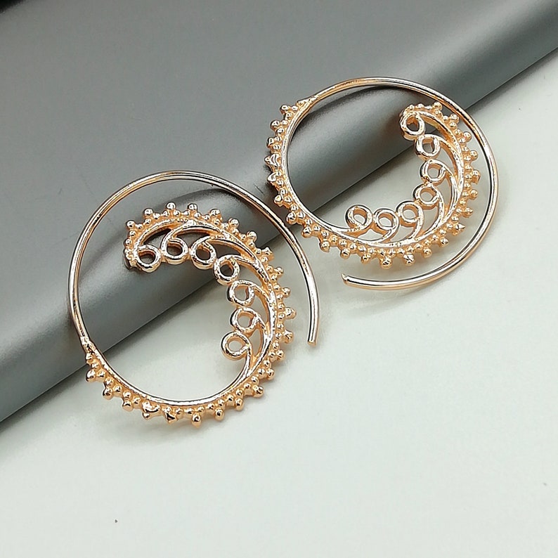 May include: A pair of gold-toned hoop earrings with a delicate, swirling design. The earrings are made of metal and have a textured finish.
