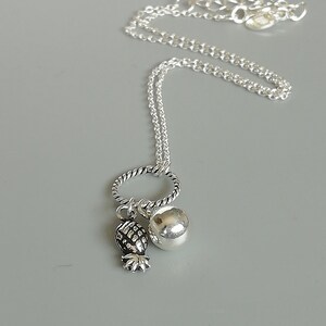 May include: A silver necklace with a twisted circle charm, a small silver pineapple charm, and a silver ball charm.