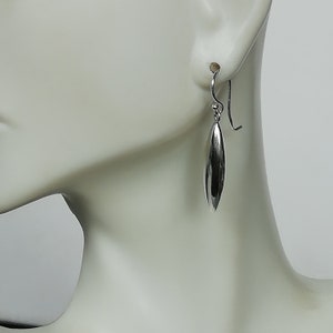 May include: Silver dangle earrings with a smooth, oval-shaped pendant.