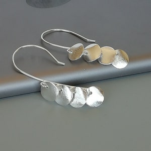 May include: Silver dangle earrings with multiple round discs hanging from a hook.
