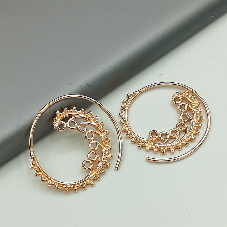May include: A pair of gold-toned hoop earrings with a decorative, swirling design. The earrings are made of metal and have a delicate, intricate pattern.