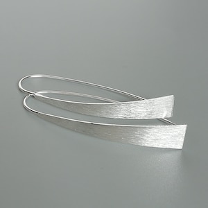 May include: A pair of silver dangle earrings with a brushed finish. The earrings are long and thin, with a curved shape.