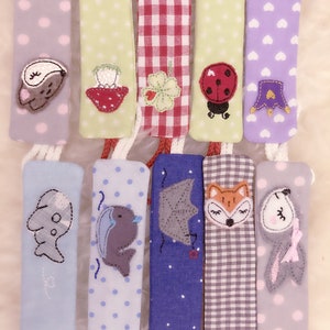 May include: Set of ten fabric strips with embroidered designs. The strips are in various colors and patterns, including polka dots, gingham, and hearts. Each strip features a different embroidered animal or design, such as a mouse, a strawberry, a ladybug, a fox, and a fish.