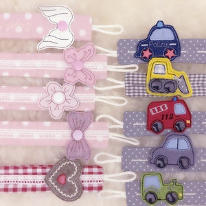May include: Set of 10 colorful fabric baby teethers with various designs, including a heart, wings, flowers, and different vehicles. The teethers are made of soft fabric and have a loop for attaching to a stroller or car seat.
