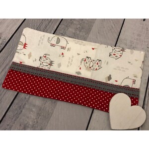 Op de afbeelding: Een witte kussensloop met een rode en witte stippenrand. De kussensloop heeft een grijs en wit patroon van olifanten en andere dieren. De kussensloop is versierd met een grijze kant.