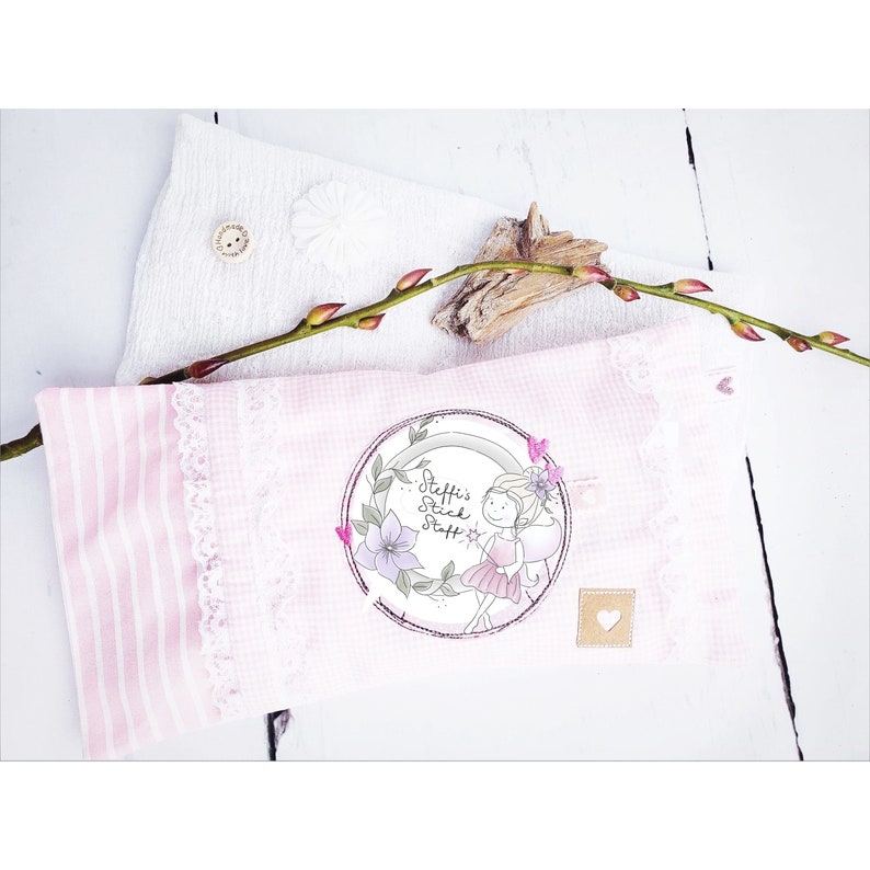 May include: A pink and white striped pillow with a white lace trim. The pillow has a circular patch with a drawing of a fairy with wings and a wand. The text on the patch reads "Steffi's Stick Staff".