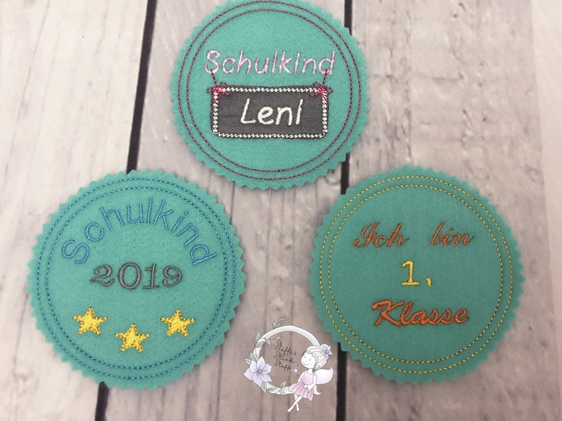 Pode incluir: Tr&ecirc;s c&iacute;rculos de feltro com texto bordado. O primeiro c&iacute;rculo &eacute; azul turquesa com o texto "Schulkind 2019" e duas estrelas douradas. O segundo c&iacute;rculo &eacute; azul turquesa com o texto "Schulkind" e um quadro-negro com o texto "Leni". O terceiro c&iacute;rculo &eacute; azul turquesa com o texto "Ich bin 1. Klasse".