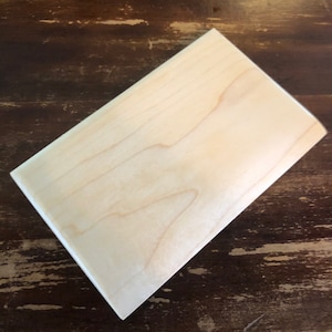 Peut inclure: Une planche à découper en bois clair et lisse. La planche est rectangulaire et présente un grain de bois naturel.