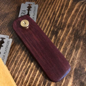 May include: A wooden razor handle with a purple stain finish. The handle has a brass knob on top. The razor blade is not included.