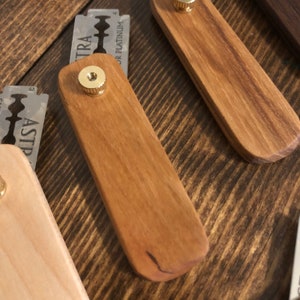May include: Two wooden razor handles with a brass knob on the top. The handles are made of different types of wood, one is a light wood and the other is a darker wood.