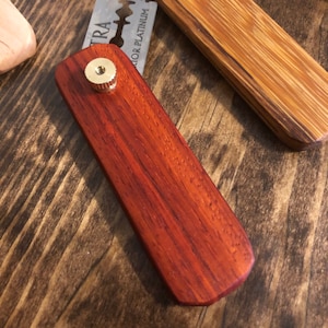 May include: A wooden straight razor handle with a brass screw. The handle is a rich reddish-brown color and has a smooth, polished finish.