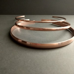 May include: Three rose gold metal choker necklaces stacked on top of each other. The necklaces are all the same width but different lengths.