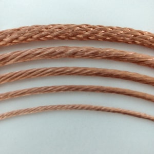 May include: Four different sizes of copper wire rope, braided and coiled, on a white background.