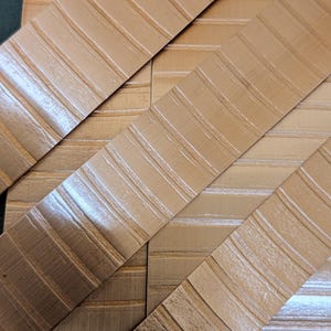 May include: A close-up shot of several tan-coloured, textured strips arranged diagonally. Each strip features a series of parallel, raised lines. The strips overlap, creating a geometric pattern.