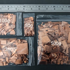 May include: Four clear plastic bags containing copper pieces of different shapes. The bags are labelled with weights: 100g, 50g, 250g, and 500g. A metal ruler is positioned above the bags for scale.