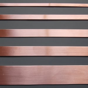 May include: Five horizontal strips of copper metal, each with a brushed finish, are arranged against a dark grey background.