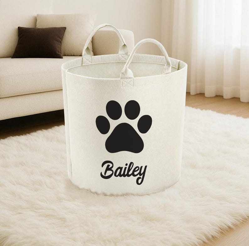 A white tote bag with a black paw print and the name "Biley" printed on it, placed on a white shag rug in a living room.
