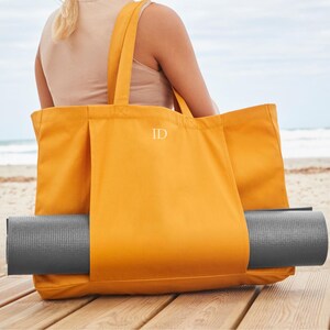 a woman sitting on a beach holding a yellow tote bag