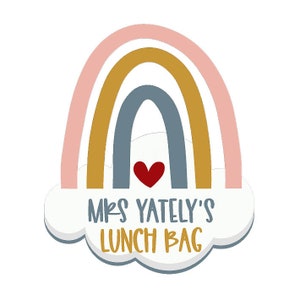 May include: A colorful rainbow design with a red heart and the text "MRS YATELY'S LUNCH BAG" in a playful font. The rainbow features pastel pink, gold, and blue arches, set against a white cloud background.